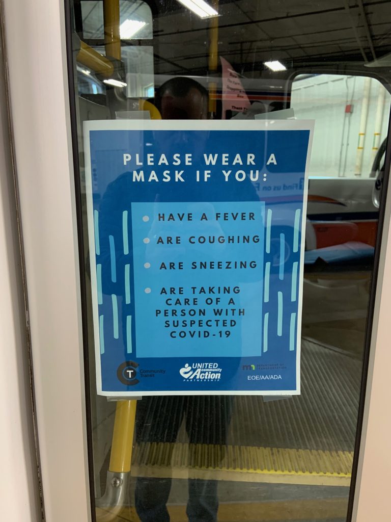 signage on a UCAP Bus sign reads "Please wear a mask if you have a fever, are coughing, are sneezing, are taking care of a person with suspected COVID-19