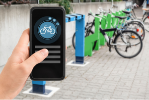 photo of electric bikes docked in their station and hand holding a smart phone with a bike icon displayed on the screen